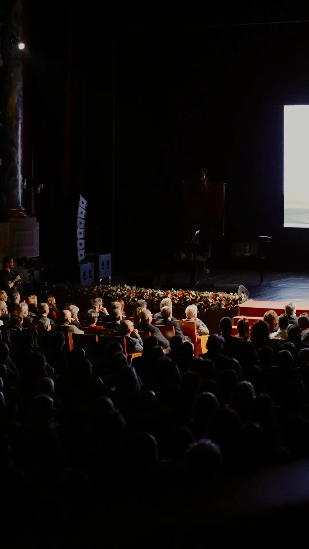 A large group of people sitting in front of a screen.