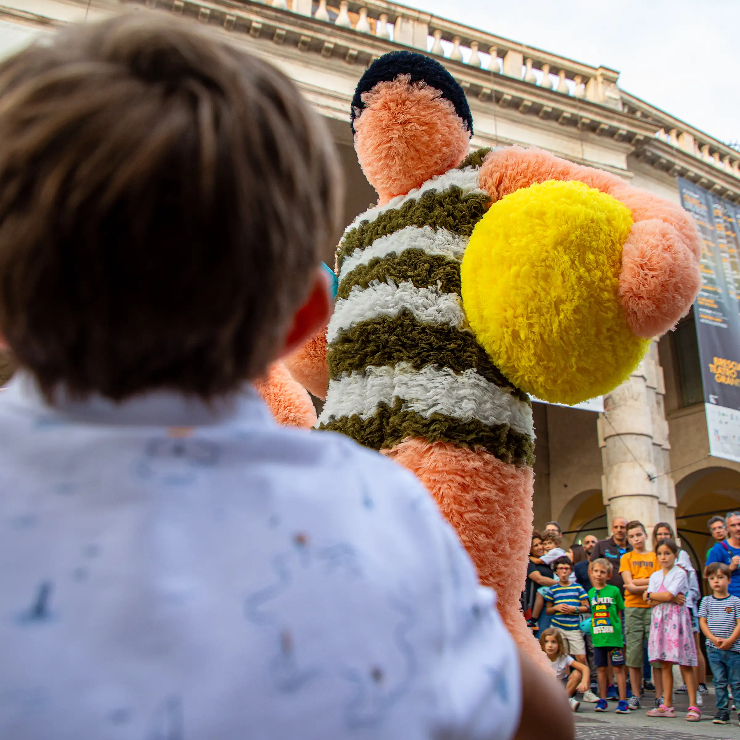 A young boy watching a large teddy bear with a ball in his hand.